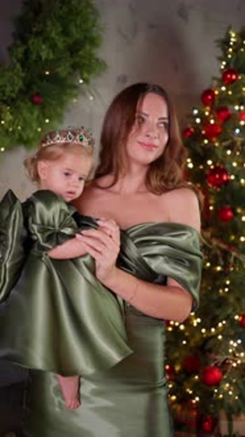 Woman Holds Child in Front of Christmas Tree