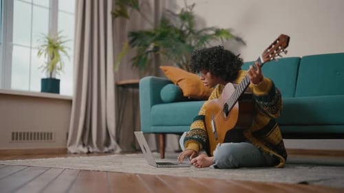 Woman Playing Guitar While Using Laptop at Home