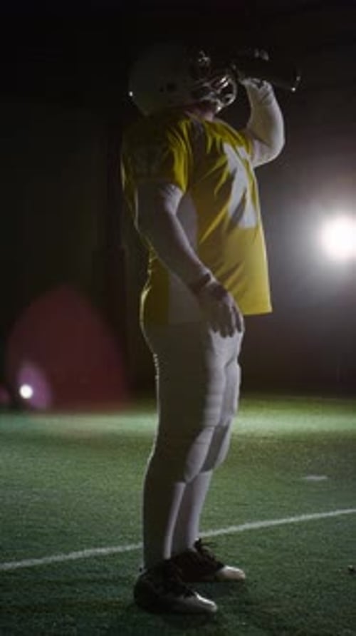 Muskulöser Gridiron-Fußballspieler trinkt während der Spielpause Wasser