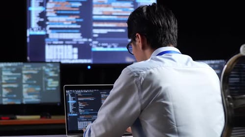 Close Up Back View Of Programmer Writing Code By A Laptop Using Multiple Monitors Showing Database