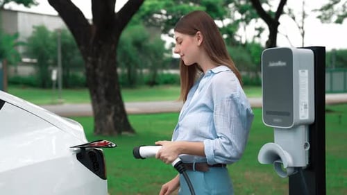 Woman recharging battery for electric car during road trip. Exalt