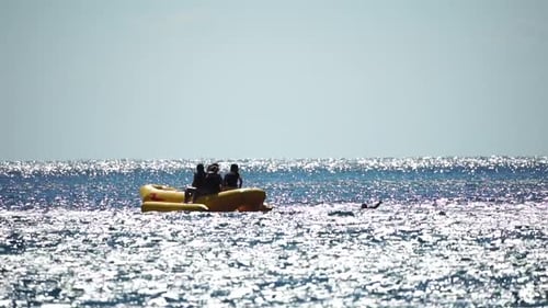 People Enjoying Banana Boat Ride on Sunny Ocean Day