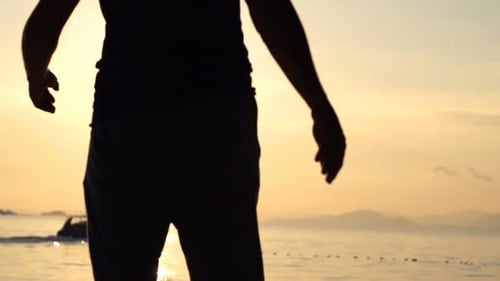 Man walks silhouetted on exotic beach at sunset in golden slow motion