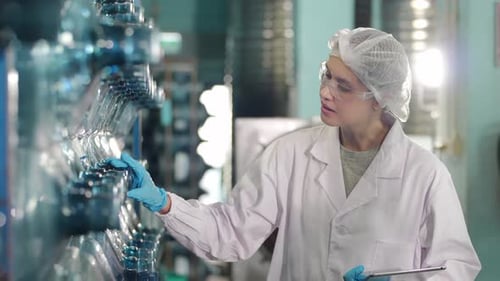 Une travailleuse inspecte la qualité de l'eau et des bouteilles dans une usine de production d'eau potable