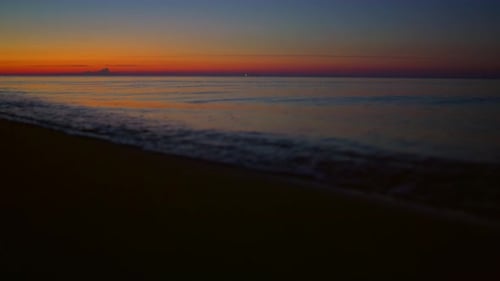 Golden sunrise reflecting on dark sand beach waves splashing in slow motion