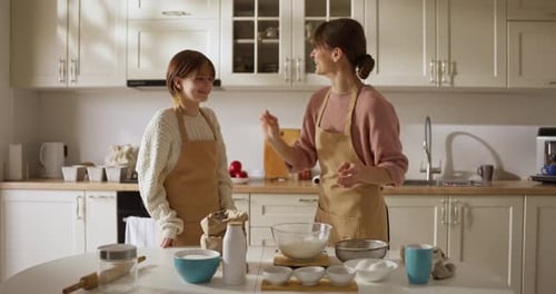 Mom Puts Her Finger in Flour and Then on Her Daughter Face During Fun Baking Game in Kitchen at Home