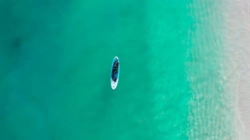 Aerial Top View of a Woman on a Surfboard in the Turquoise Waters of the Maldives