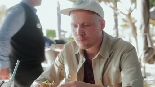 A Man Eats a Chicken Sandwich Sitting in a Cafe in the Fresh Air