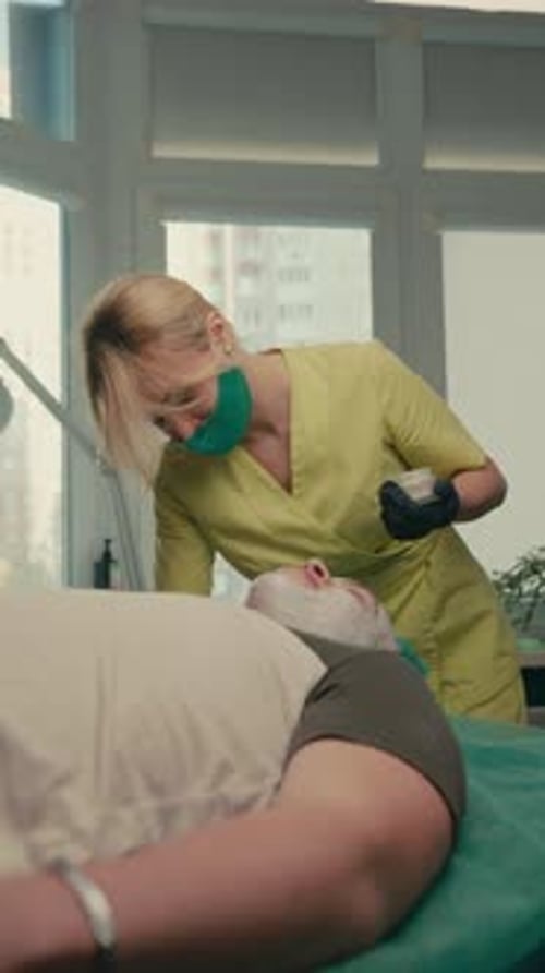 The cosmetologist performs cream peeling on the patient's problematic skin with acne, vertical frame