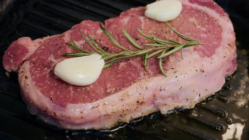 Close up of steak cooking on a grill pan topped with fresh rosemary