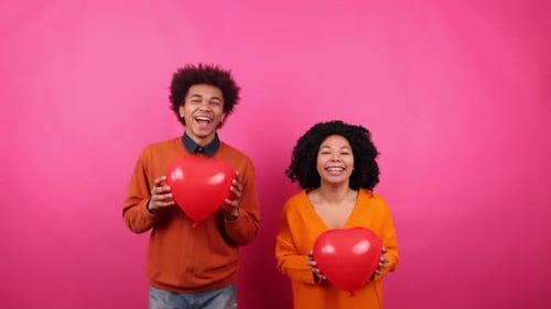 Cheerful Couple Holding Heart Balloons on Pink Background