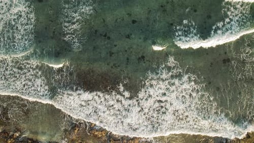 Aerial view of ocean waves breaking over a shallow coral reef in evening light