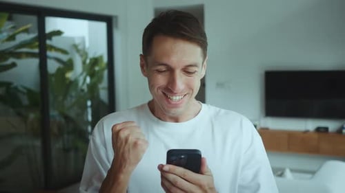 Excited Man Celebrates Good News on Smartphone at Home