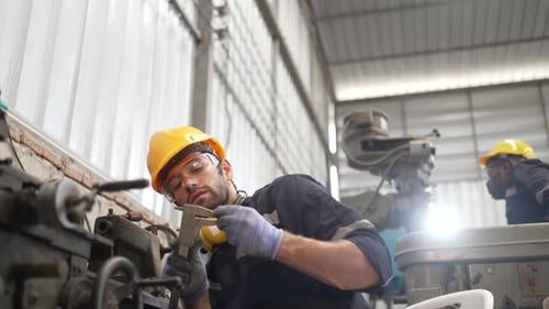 Blue collar workers at machine shop with welding robot arm.