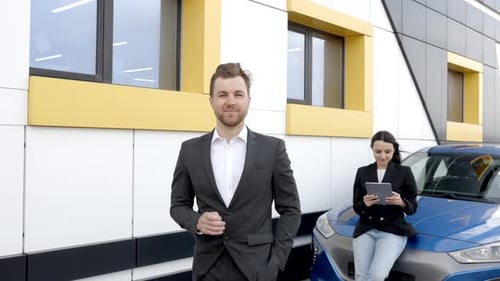 Confident male shop assistant in formal clothes holding key and looking at camera at automobile car