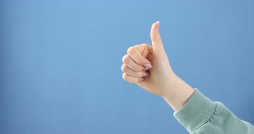 Woman turning thumbs up into thumbs down gesture on blue background, closeup