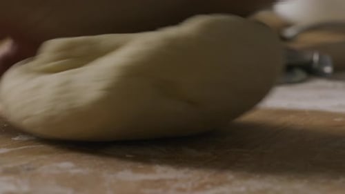 Nahaufnahme von Händen, die Teig auf einem mit Mehl bedeckten Küchentisch kneten