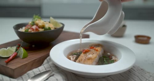 Chef preparing and pouring broth over fish dish