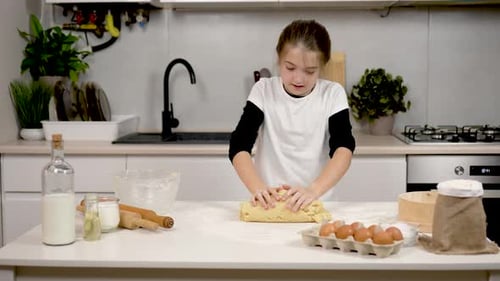 Little Girl Vigorously Kneads Dough with Hands Making Effort in Beautiful Cozy Kitchen Child