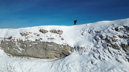 Solo hiker walking on the mountain ridge. Vast winter mountain landscape full of snow.