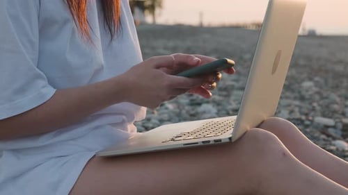 Close Up of Woman Working with Laptop and Mobile Phone on the Beach By the Sea During Sunset Female