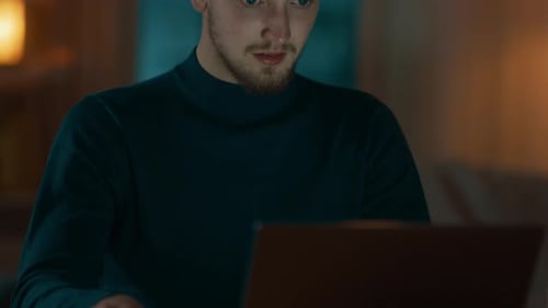 Evening at Home: Portrait of Handsome Man Sitting at His Desk Working on a Laptop. Smiling Freelanc