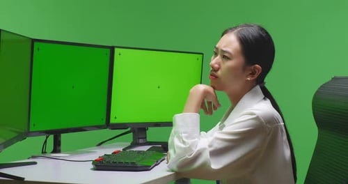 Asian Woman Thinking While Working With Mock Up Multiple Computer Monitor In Green Screen Studio