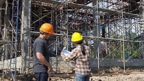 Construction manager and engineer discussing and checking plans on construction site.