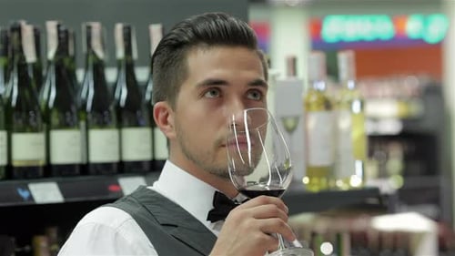 Young Man Inspecting Red Wine in Liquor Store