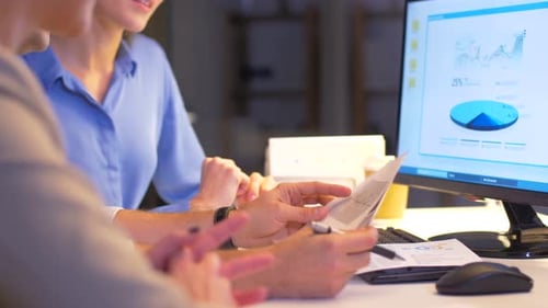 Business team analyzes charts and data on computer screen late at night office