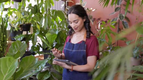 Smiling latin woman florist works on digital tablet in her flower shop
