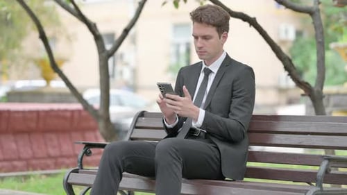 Young Adult Using Smartphone on Park Bench