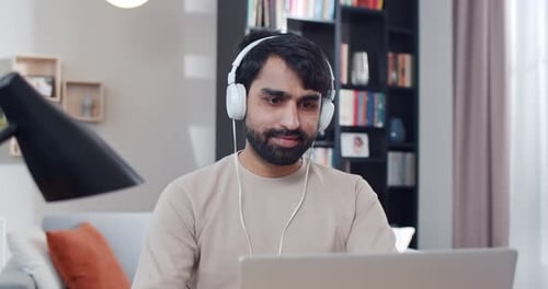 Close Up of Arabian Young Handsome Man in Headphones Sitting at Table Listening to Music and Working