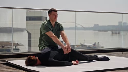 Male Therapist Guiding Patient Through Outdoor Physiotherapy Session with City Skyline Backdrop