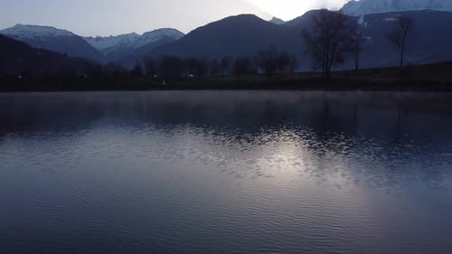 Flying close to the water over the Passy lake with the sun starting to show over the Mont Blanc, hig