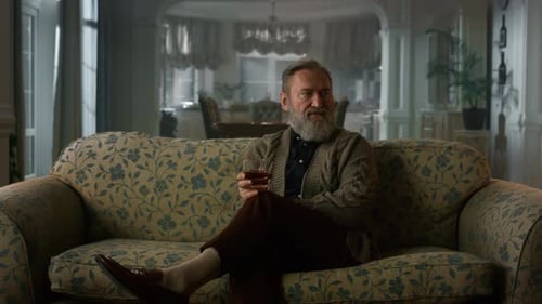 Senior Man Relaxing on Couch with Glass of Whiskey