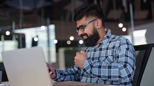 Businessman Celebrates Success with Phone and Laptop in Office