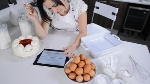 Cheerful brunette woman using tablet computer while baking cupcakes at home