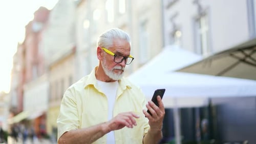 Senior Man Uses Smartphone on City Street
