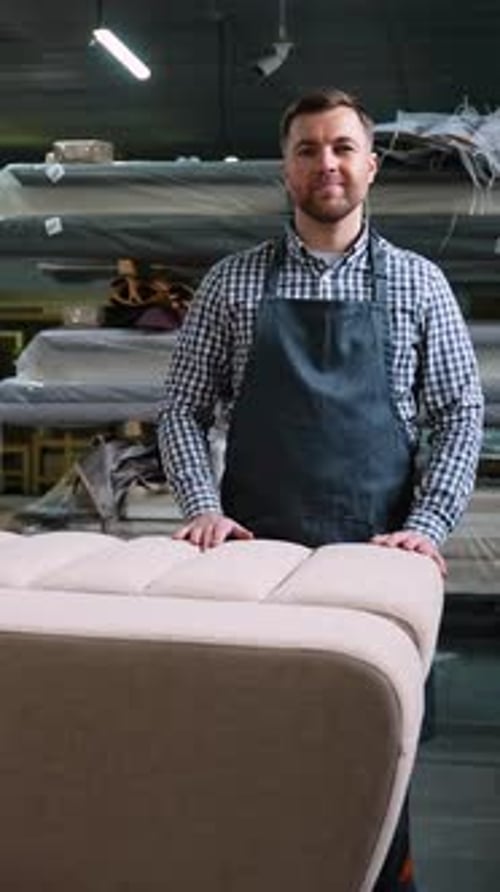 Tapicero sonriente de pie junto a un sofá terminado en el taller