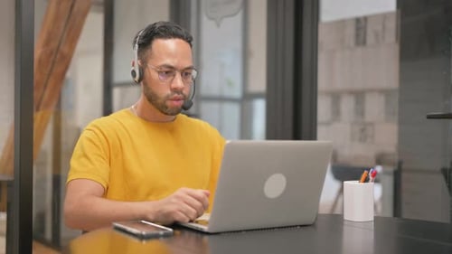 Young Adult Using Laptop and Headset in Office
