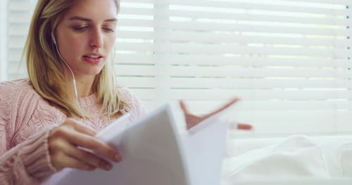 Vidéo 4K d'une jeune femme écoutant de la musique et lisant des documents sur le canapé à la maison