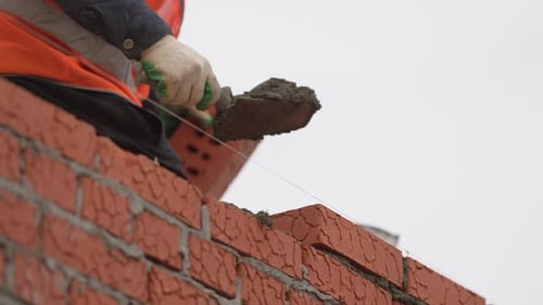 Worker Scoops Mortar Onto Brick Line Using Small Trowel