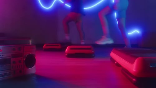 People Exercise on Step Platforms in Neon Lighting