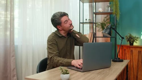 Man Typing on Laptop Massaging Stiff Neck at Desk