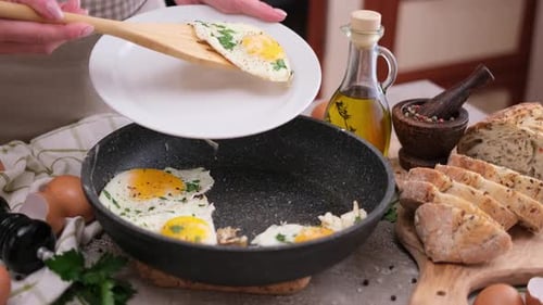 Une femme met des œufs frits de la poêle à l'assiette