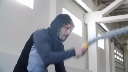 Hombre atlético haciendo ejercicio con Battle Rope en el gimnasio