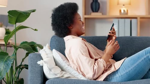 A laughing young woman texting on a phone at home