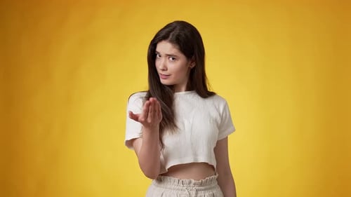Young Woman Beckons and Winks on Yellow Background