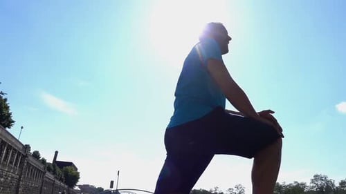 Handsome young man stretching leg muscles in city park super slow motion